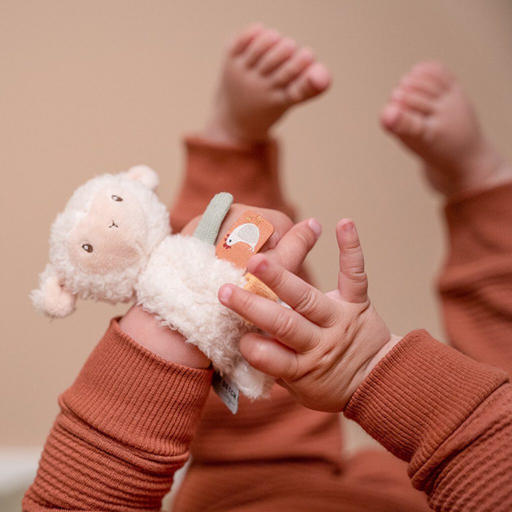 kind heeft handen en voeten in de lucht. Aan zijn hand heeft hij een pluche polsbandje met schapenkop