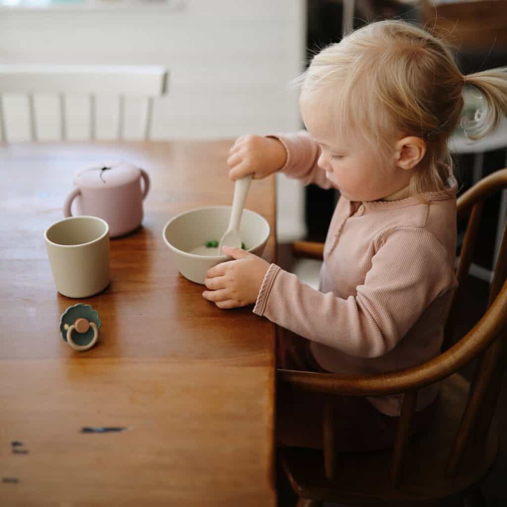 Kind zit aan tafel te eten van kinderservies
