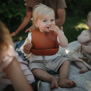 Baby met slab van Mushie baby zit te eten met roestbruine slab om